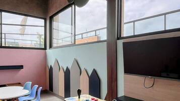 A room with a large window, a table with chairs, and a colorful arcade game.