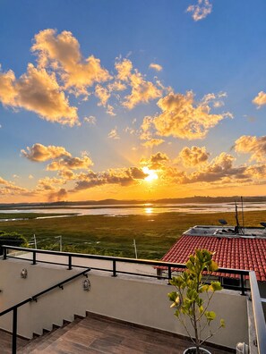 A rooftop terrace with a view of the sunset over a landscape.