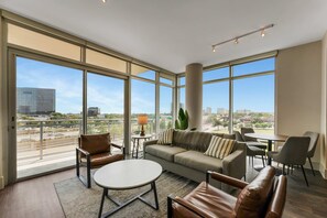 Ein großzügiger Wohnbereich mit einer Couch, Sesseln, einem Couchtisch und Blick auf die Stadt durch große Fenster.
