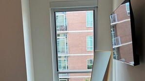 Un dormitorio con un ventanal grande, una cama, un televisor de pantalla plana en la pared y una mesita.