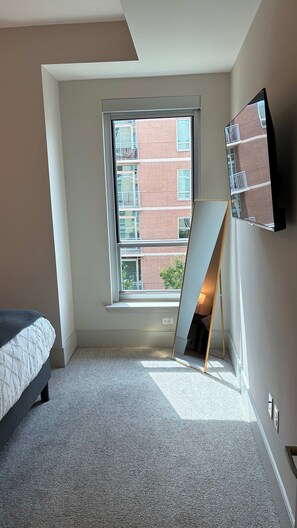 A bedroom with a large window, a bed, a flat-screen TV mounted on the wall, and a small table. - Preston Royal Single I Premium 1BR in Dallas (Dallas)