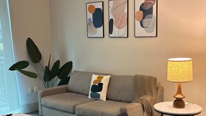 Una sala de estar con sofá, una mesa de centro redonda, lámpara y arte abstracto en la pared.