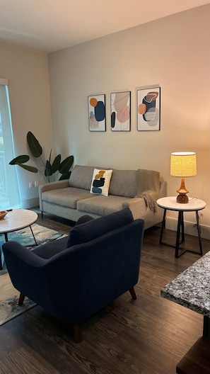 A living room with a sofa, a round coffee table, a lamp, and abstract wall art. - Preston Royal Single I Premium 1BR in Dallas (Dallas)