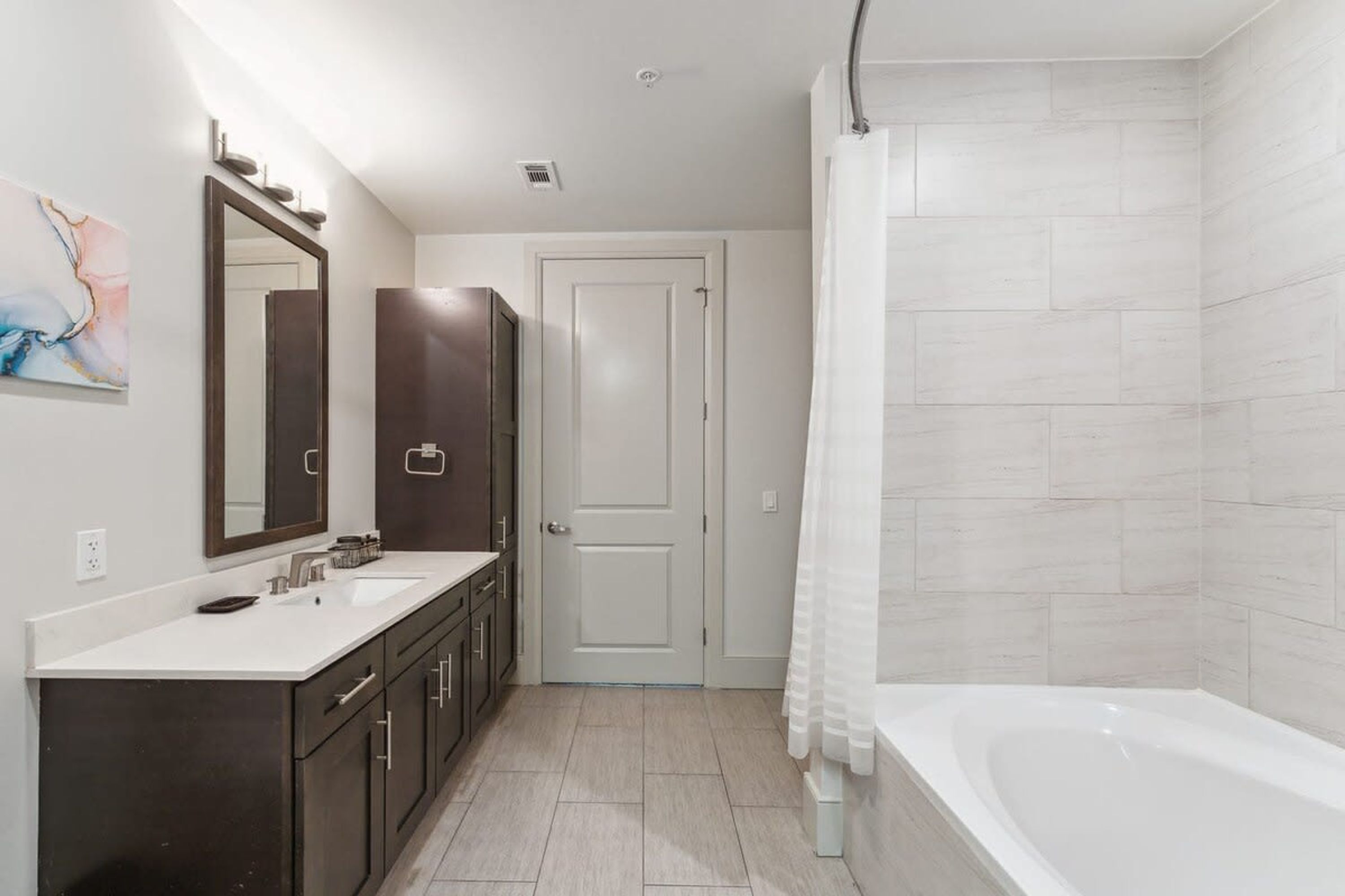 A modern bathroom with a double sink vanity, a bathtub, and a shower curtain.