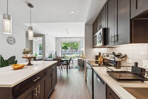 A modern kitchen with dark cabinets, a white countertop, and a dining area with a view. - Preston Douglas Single I Premium 1BR in Dallas (Dallas)