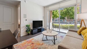 Ein modernes Wohnzimmer mit einer Couch, einem Fernseher, einem Esstisch und einem großen Fenster mit Blick ins Freie.