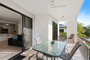 Un balcon avec une table et des chaises en verre, un ventilateur de plafond et une vue sur l’extérieur.