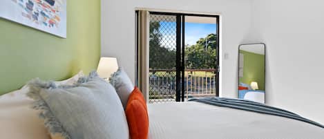 A hotel room with a bed, a nightstand, a window with a view, and a door leading to an outdoor area.