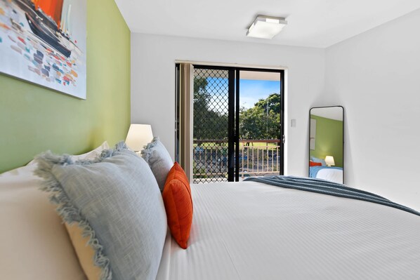 Habitación de hotel con una cama, una mesita de noche, un ventanal con vistas y una puerta que da a un espacio exterior.