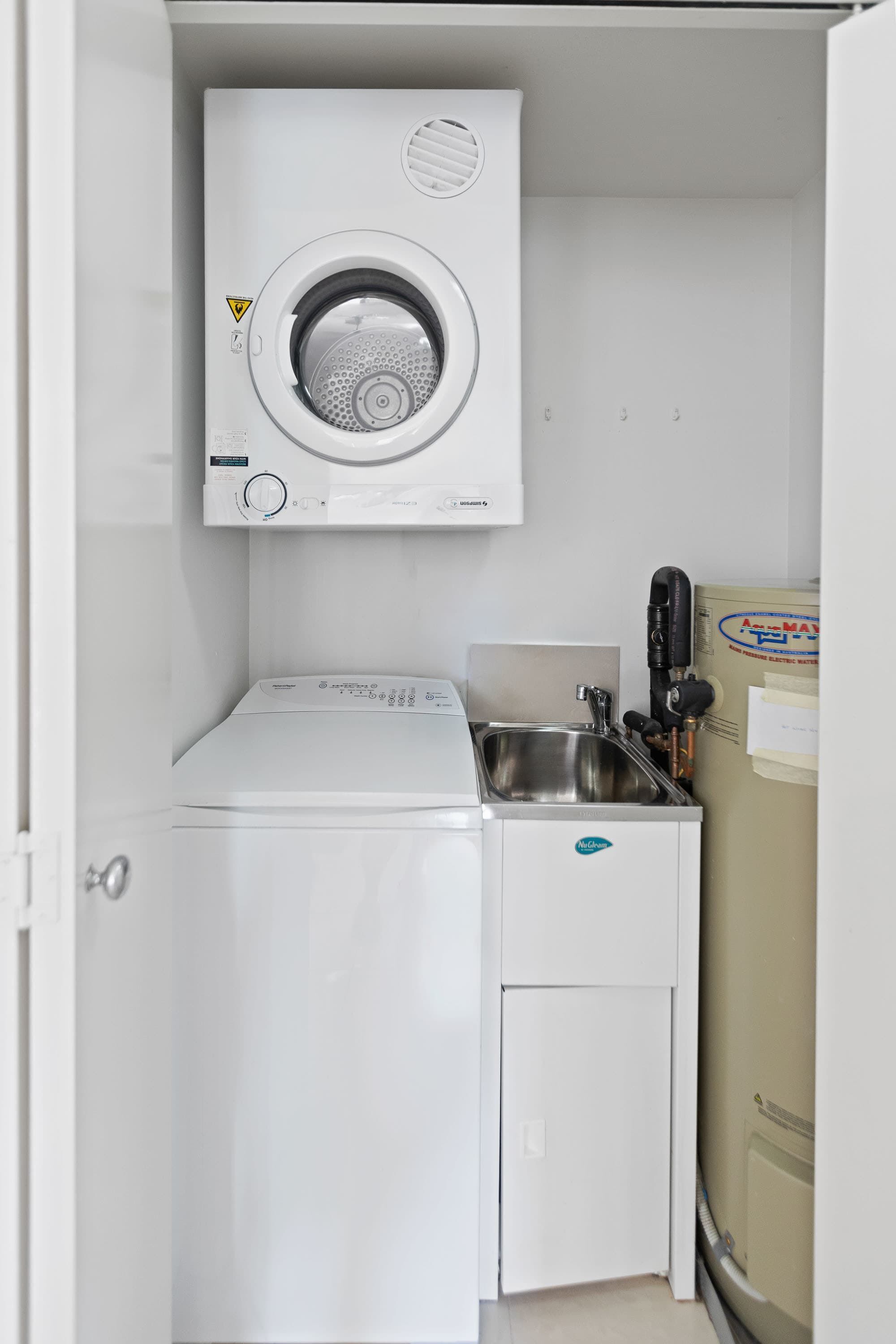 Un área de lavandería compacta con lavadora de carga frontal, secadora y lavabo.