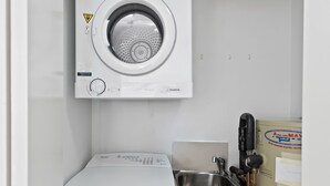 A compact laundry area with a front-loading washing machine, a dryer, and a sink. - Cairns Hideaway - Pool and Spacious (Cairns)