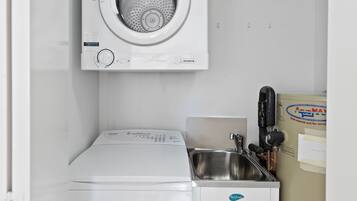 Un área de lavandería compacta con lavadora de carga frontal, secadora y lavabo.