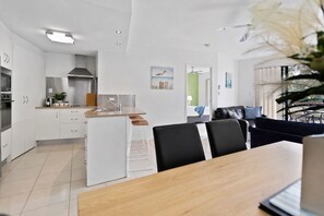 Une cuisine moderne avec des meubles blancs, un îlot central et un coin repas comprenant une table en bois et des chaises noires.