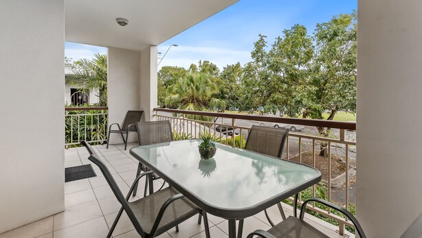 A balcony with a glass table and chairs, a ceiling fan, and a view of trees and a road. - Cairns Hideaway - Pool and Spacious (Cairns)