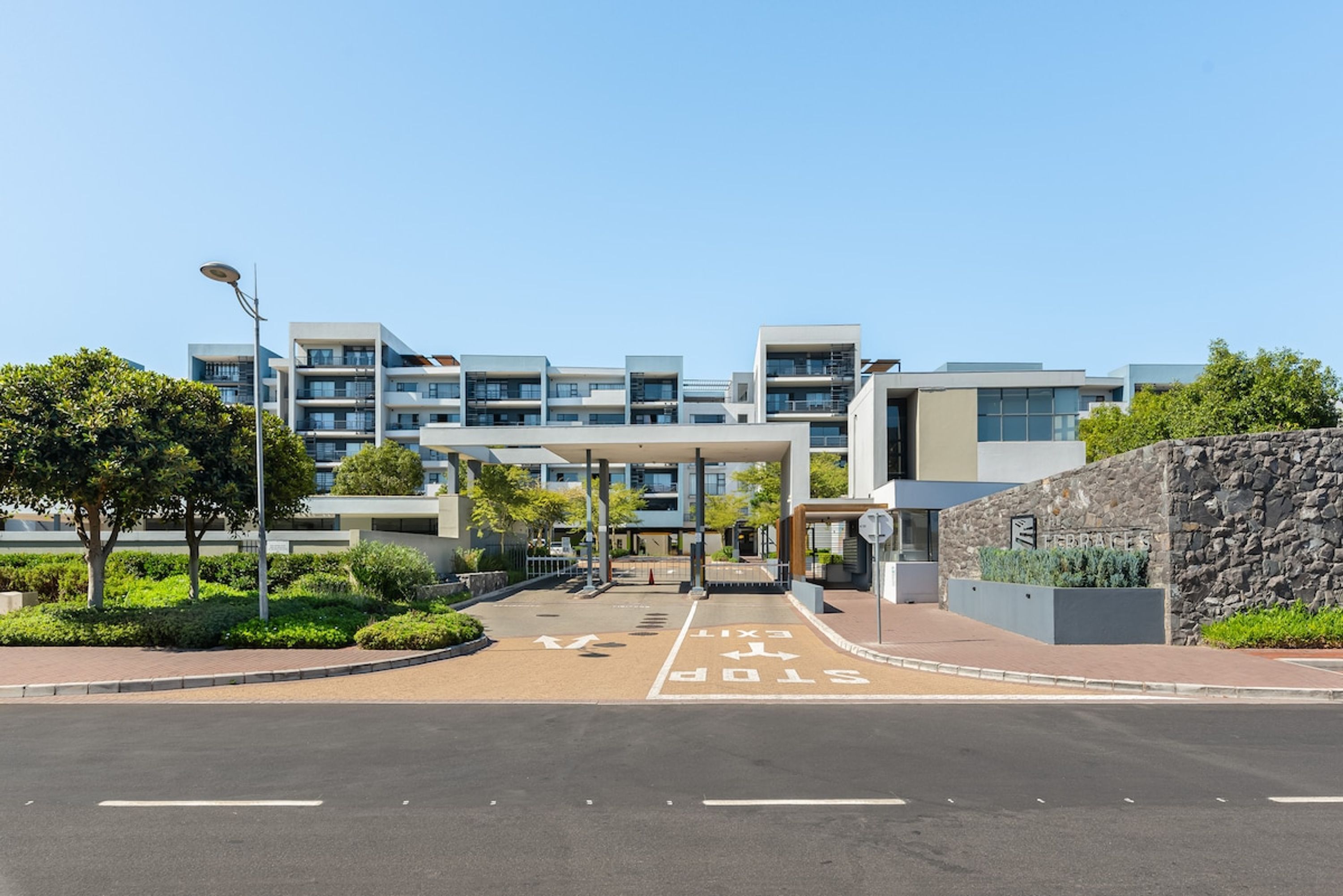 A modern building with multiple floors, a covered entrance, and a landscaped area with trees.