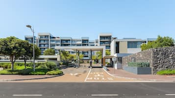 A modern building with multiple floors, a covered entrance, and a landscaped area with trees.
