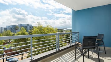 A balcony with a view of buildings and trees, a railing, and two chairs.