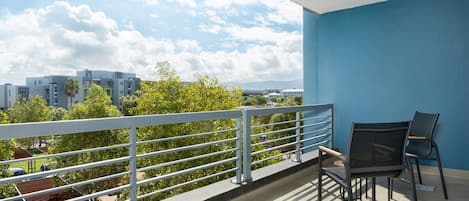 A balcony with a view of buildings and trees, a railing, and two chairs.