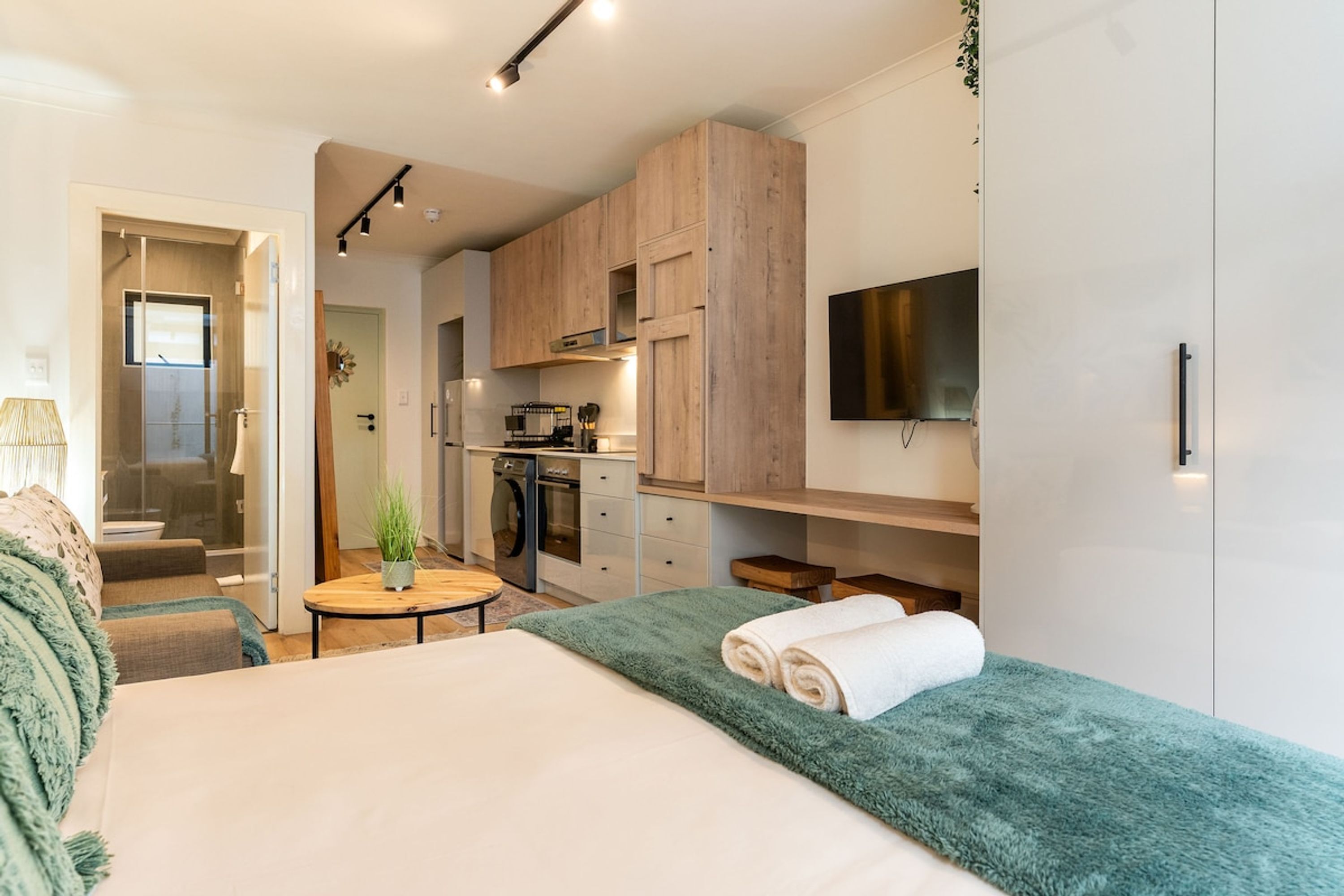 Een compacte hotelkamer met een bed, een klein rond tafeltje, een kitchenette en een aan de muur bevestigde televisie.