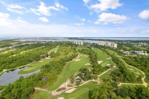 Un campo de golf con búnkeres, zonas de agua y una gran masa de agua al fondo.
