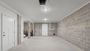 A spacious, unfinished basement with concrete walls, a door, and a ceiling light fixture. - Over the Dunes at Lost Key Villas (Pensacola)
