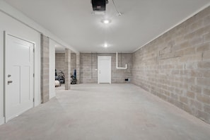 A spacious, unfinished basement with concrete walls, a door, and a ceiling light fixture. - Over the Dunes at Lost Key Villas (Pensacola)