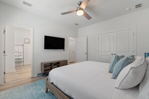 A bedroom with a bed, a TV, a ceiling fan, and a door leading to a bathroom. - Over the Dunes at Lost Key Villas (Pensacola)