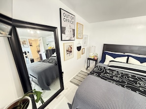 Ein Schlafzimmer mit einem großen Spiegel, einem Bett mit gemusterten Betttextilien, einem Nachttisch mit Lampe und einem gerahmten Bild an der Wand.