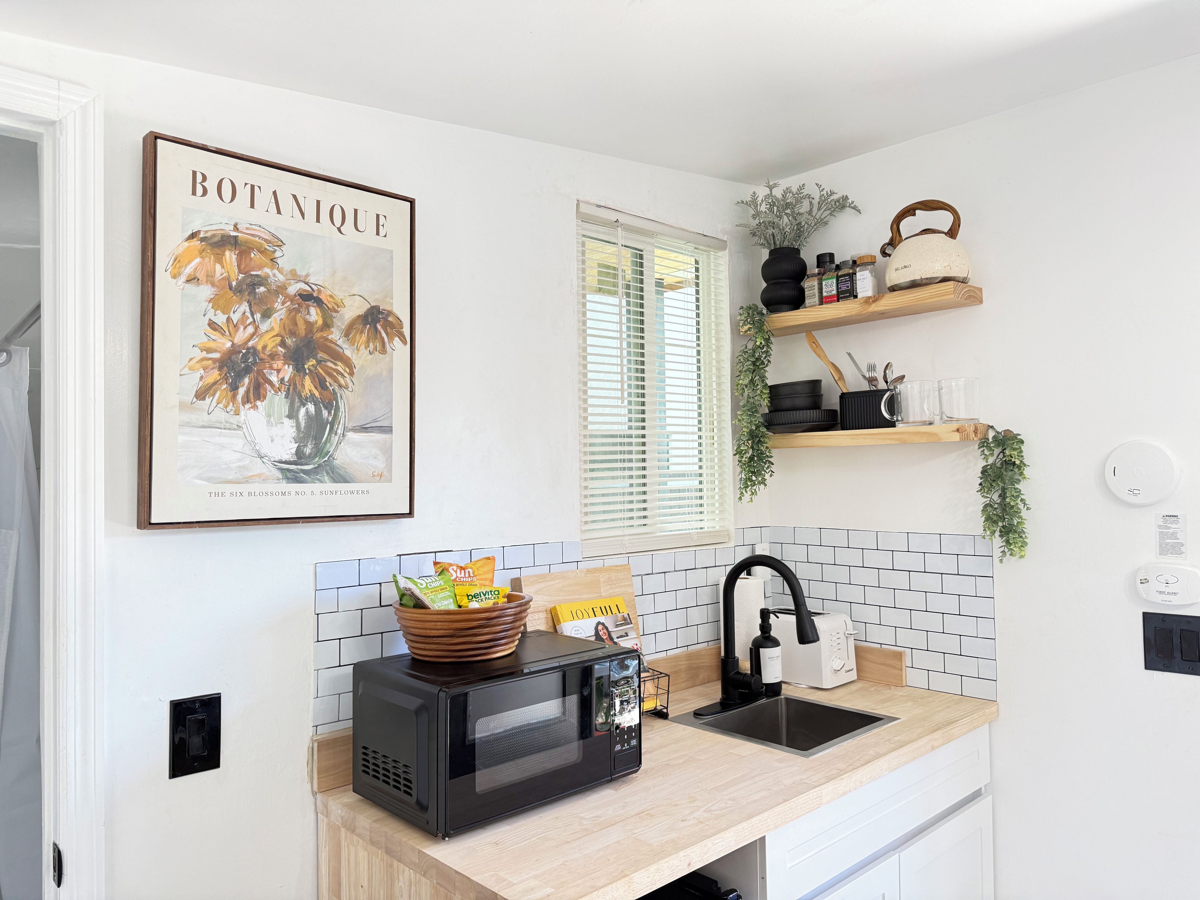A kitchen with a microwave, sink, and a framed botanical print on the wall.