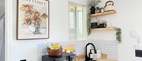 A kitchen with a microwave, sink, and a framed botanical print on the wall.