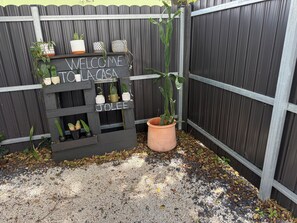 Een houten bord met de tekst 'WELCOME TO LA CASA' en 'JOLEE', omringd door potplanten.