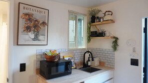 A kitchen with a microwave, a sink, and a shelf with kitchen items. There's a framed botanical print on the wall. - Private Boho Tiny Home and Retreat with Monthly Stay + Parking (Miami)