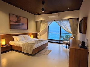 Habitación de hotel con una cama grande, lámparas de noche, un escritorio y vistas al mar a través de las ventanas.