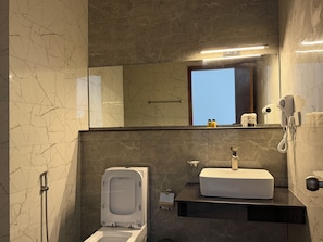 Un baño con inodoro, bidé, lavamanos y un espejo que refleja una ventana.