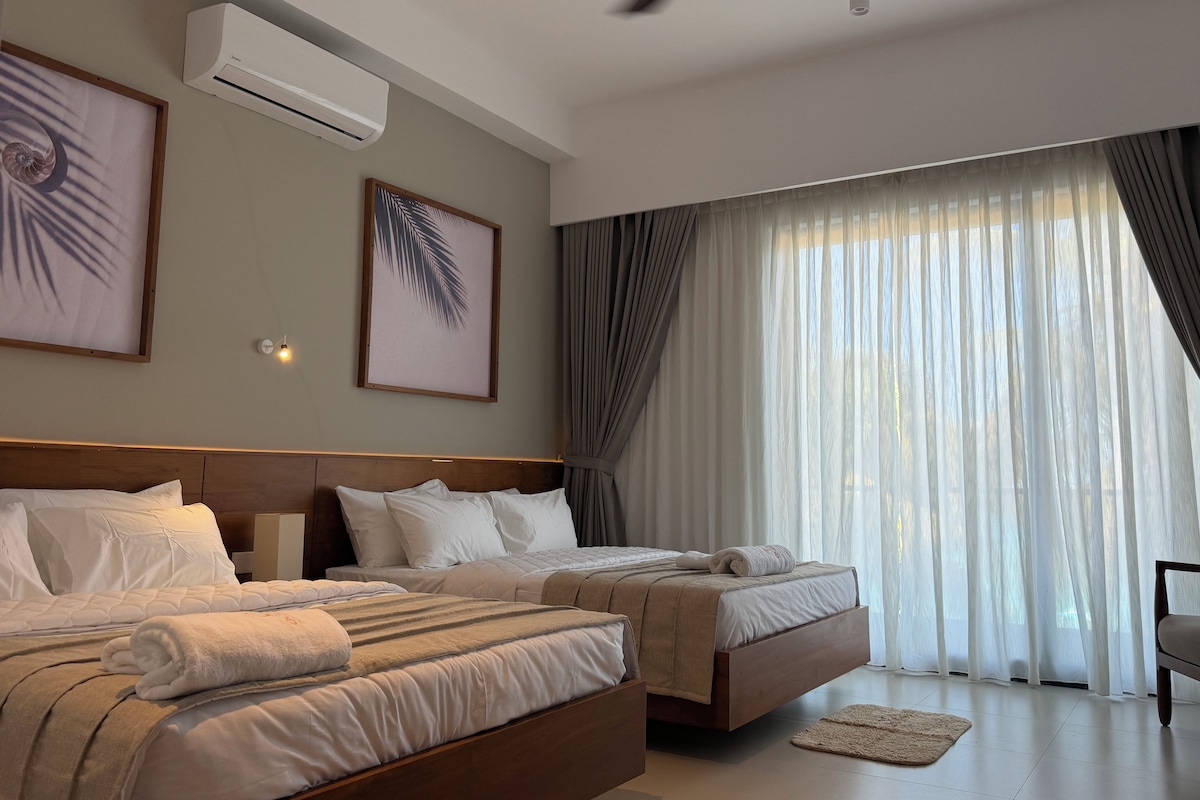 Una habitación de hotel con cama, dos mesitas de noche, ventilador de techo y una ventana grande con cortinas.