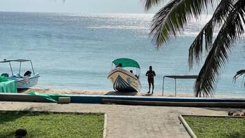 Un chemin pavé mène à une plage où se trouvent un bateau et une personne debout près de l’eau.