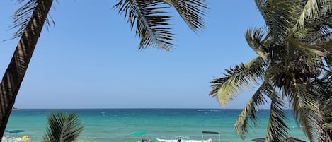 Una playa con dos barcos, palmeras y un cielo azul despejado.