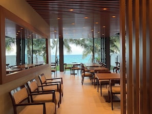 En restaurang med utsikt över havet, med träbord och stolar samt en modern takdesign.