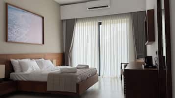 A hotel room with a bed, a desk, a chair, a ceiling fan, an air conditioning unit, and a large window with curtains.