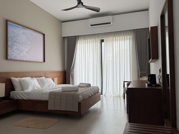 A hotel room with a bed, a desk, a chair, a ceiling fan, an air conditioning unit, and a large window with curtains.