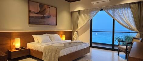 A bedroom with a bed, bedside lamps, a ceiling fan, a large window with curtains, and a painting on the wall.