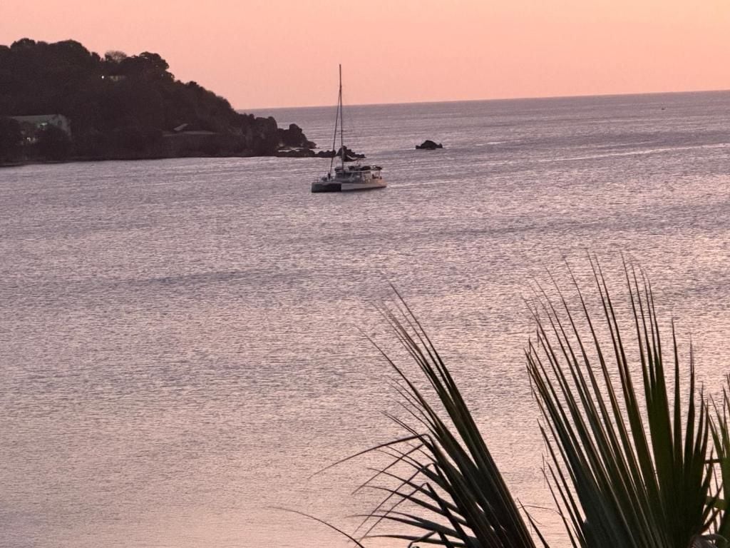 A coastal scene with a sailboat on the water and a rocky shoreline in the background.