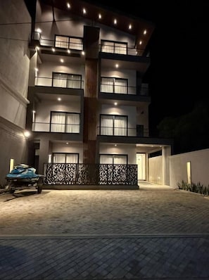 Un edificio de varios pisos con balcones, una entrada cubierta y un camino de acceso pavimentado.