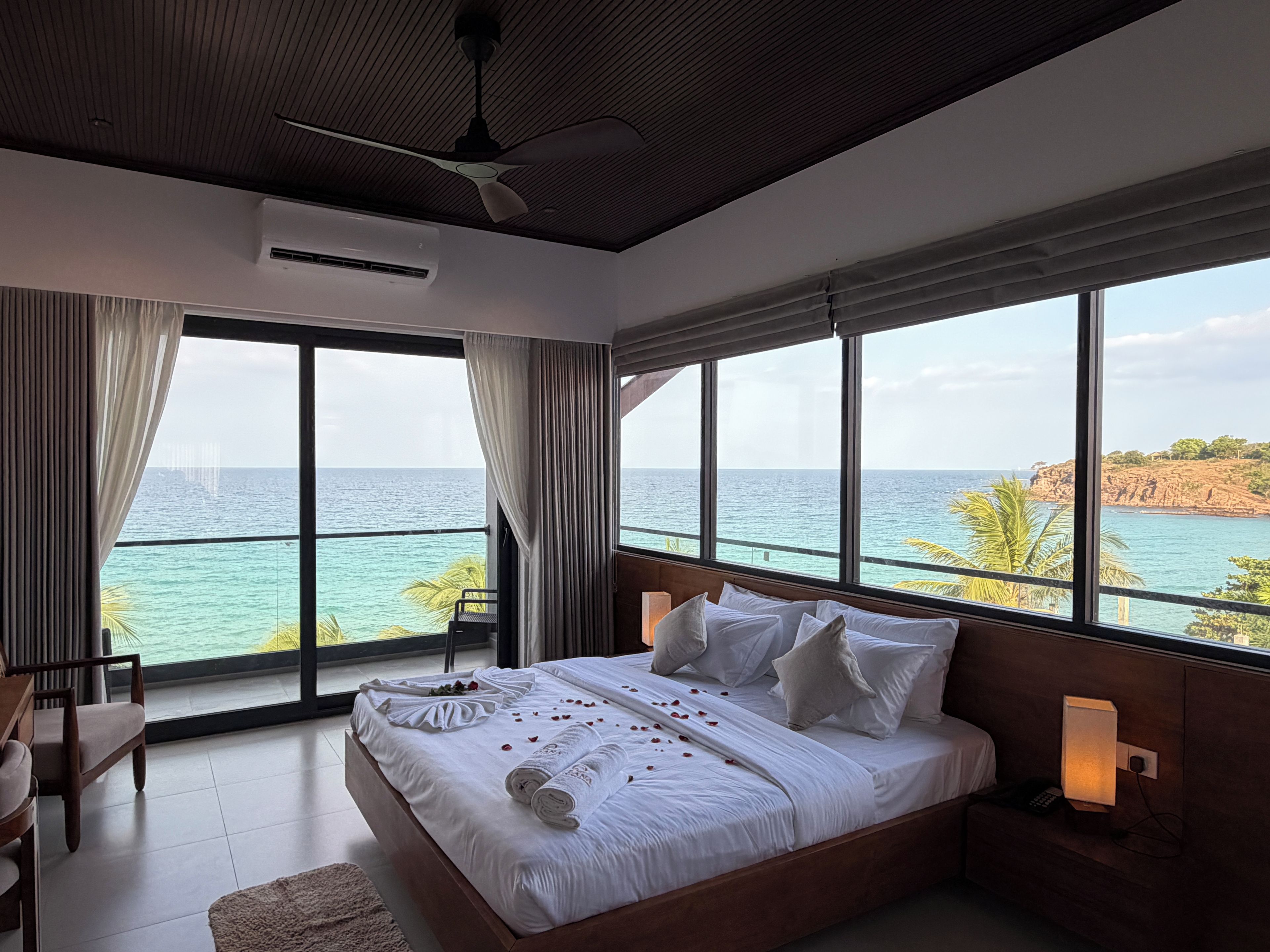 Quarto com uma cama grande, ventilador de teto e vista para o mar.