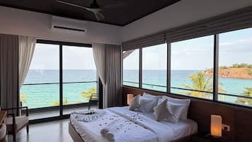 Quarto com uma cama grande, ventilador de teto e vista para o mar.