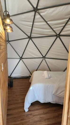 A tent with a geometric wall pattern, a wooden floor, a bed with white bedding, and a hanging light fixture.