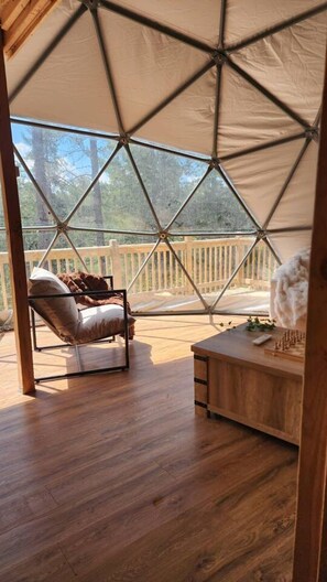 A tented room with a wooden floor, a cushioned chair, and a wooden table with a chess set.