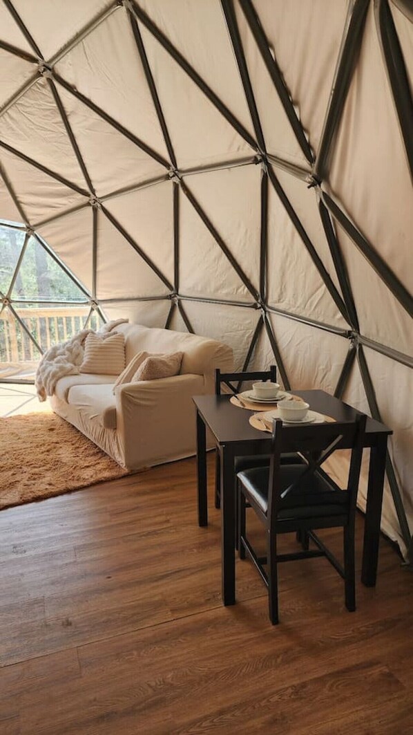 A tent with a wooden floor, a sofa, and a table with chairs.