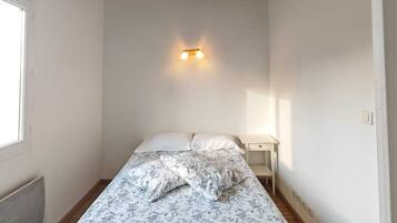 Une chambre à coucher comprenant un lit, une table de chevet, une lampe fixée au mur et des poutres apparentes.