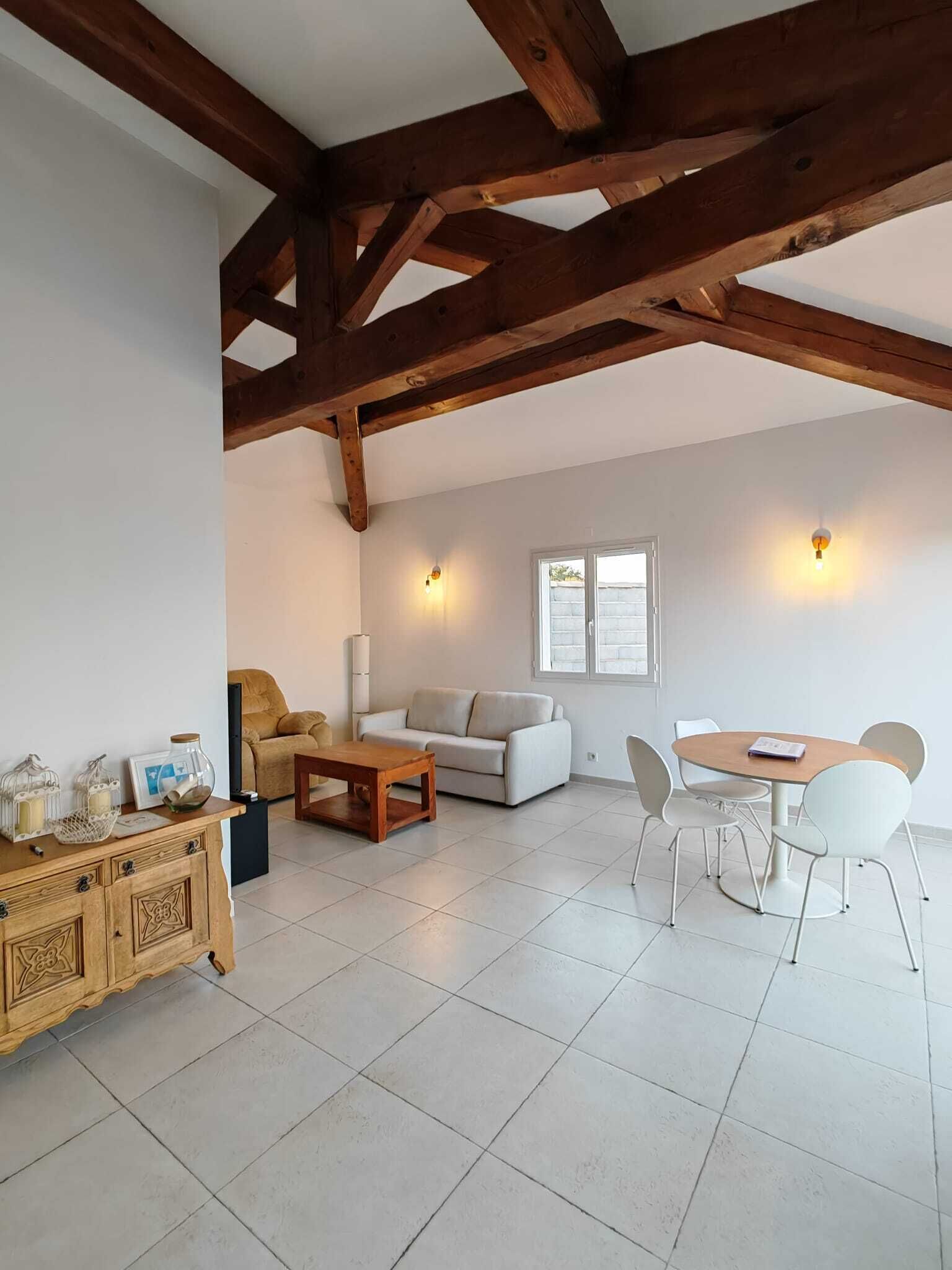 A spacious living area with a high ceiling, wooden beams, a dining table with chairs, a sofa, and a cabinet with decorative items.